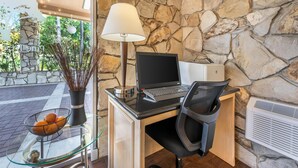 A modern office space with a stone wall, a desk with a laptop, a chair, a lamp, a vase with plants, and a glass table with a fruit bowl. - Best Western Pine Tree Motel (Chino)