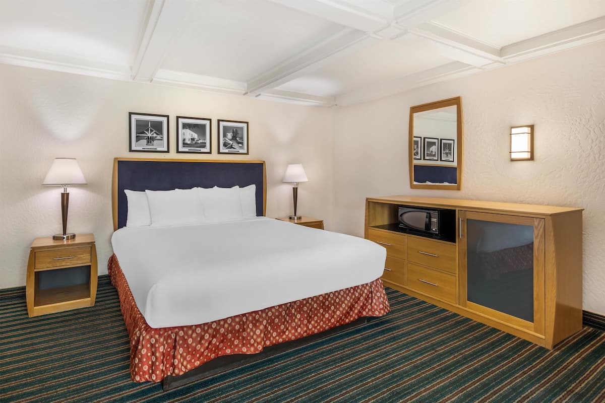 Ett hotellrum med en stor säng, två sängbord, en byrå i trä och inramade tavlor på väggen.