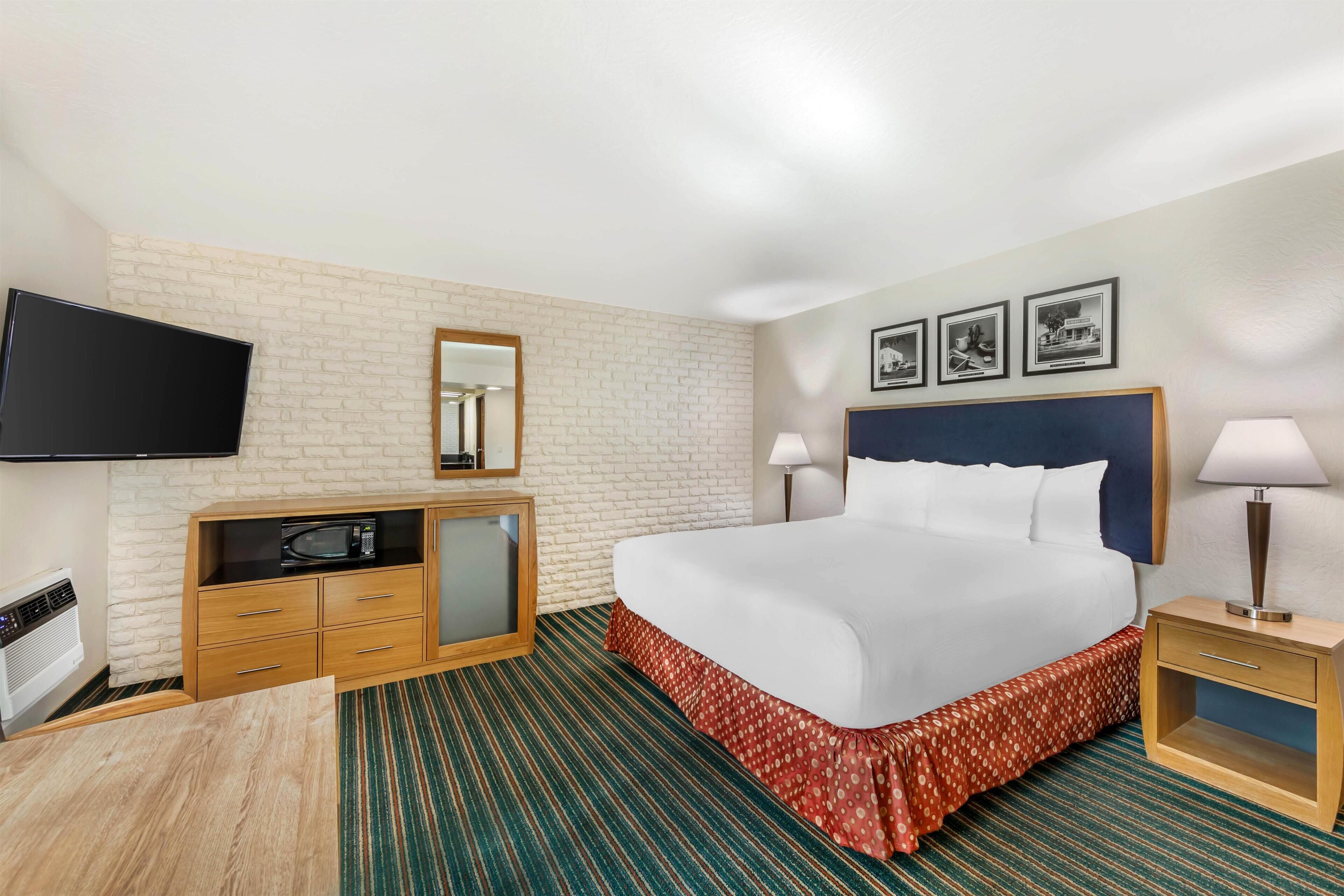 Une chambre d’hôtel équipée d’un lit, d’une télévision, d’une commode, d’un four à micro-ondes, d’une lampe et d’un tableau au mur.