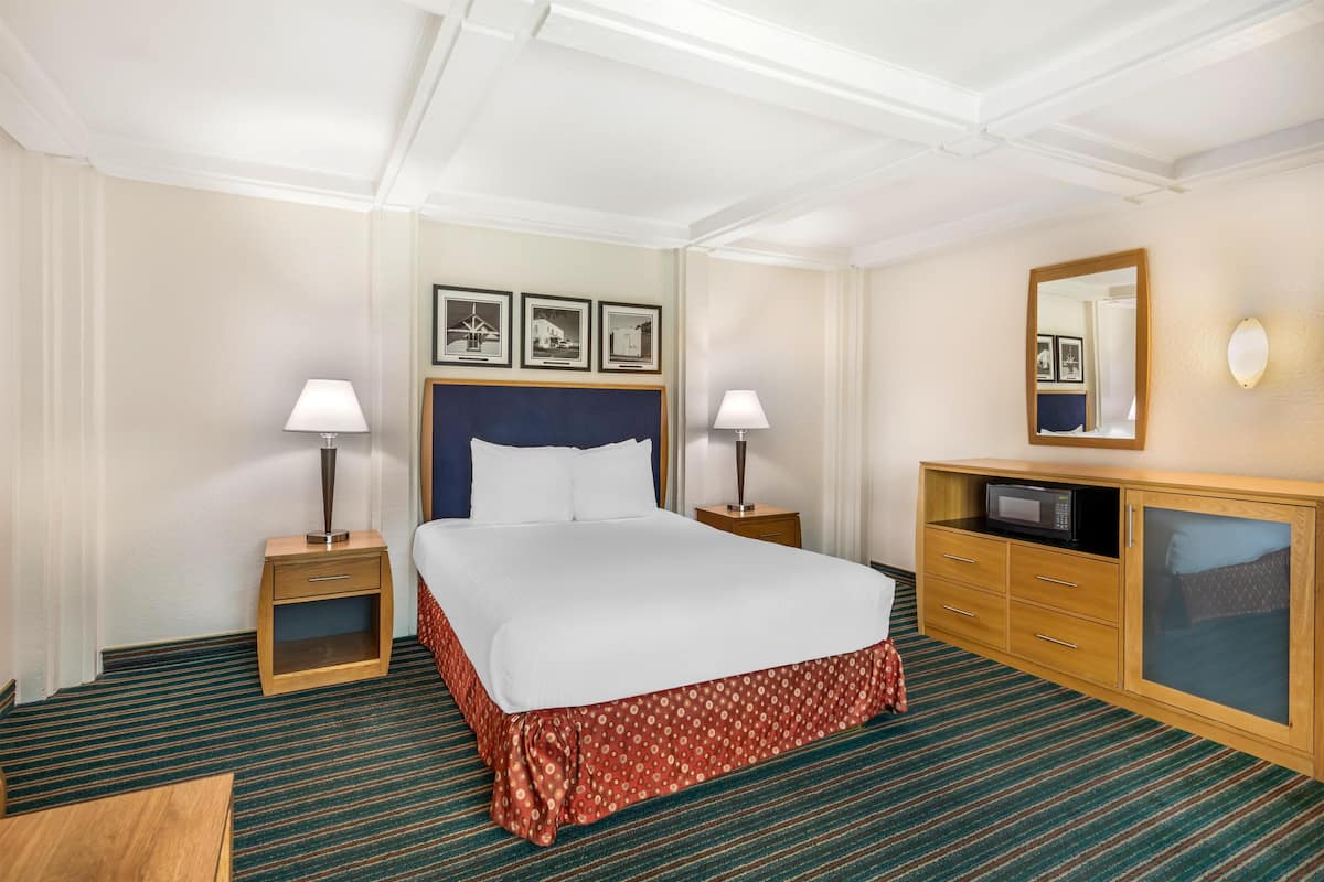 Ett hotellrum med en säng, två sängbord, en byrå, en spegel och inramade tavlor på väggen.