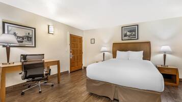 Quarto de hotel com cama, escrivaninha, cadeira, duas luminárias de cabeceira e duas imagens emolduradas nas paredes.
