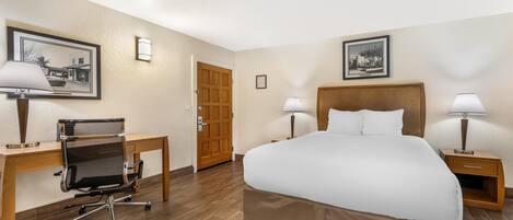 Quarto de hotel com cama, escrivaninha, cadeira, duas luminárias de cabeceira e duas imagens emolduradas nas paredes.