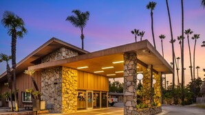 A hotel with a stone facade, a covered entrance, and palm trees in the background. - Best Western Pine Tree Motel (Chino)