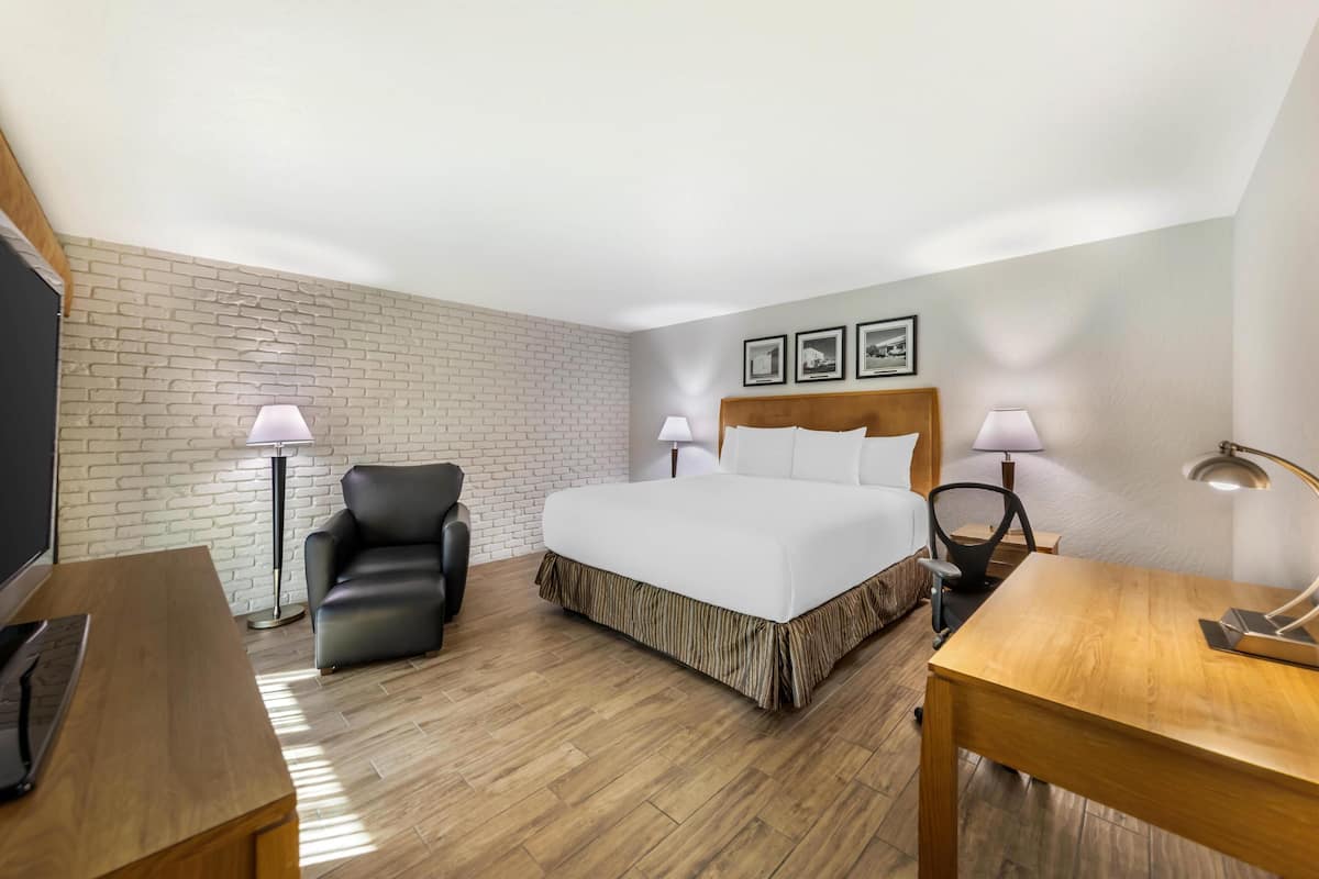 Ett hotellrum med en säng, ett skrivbord, en stol, en tv och två lampor.