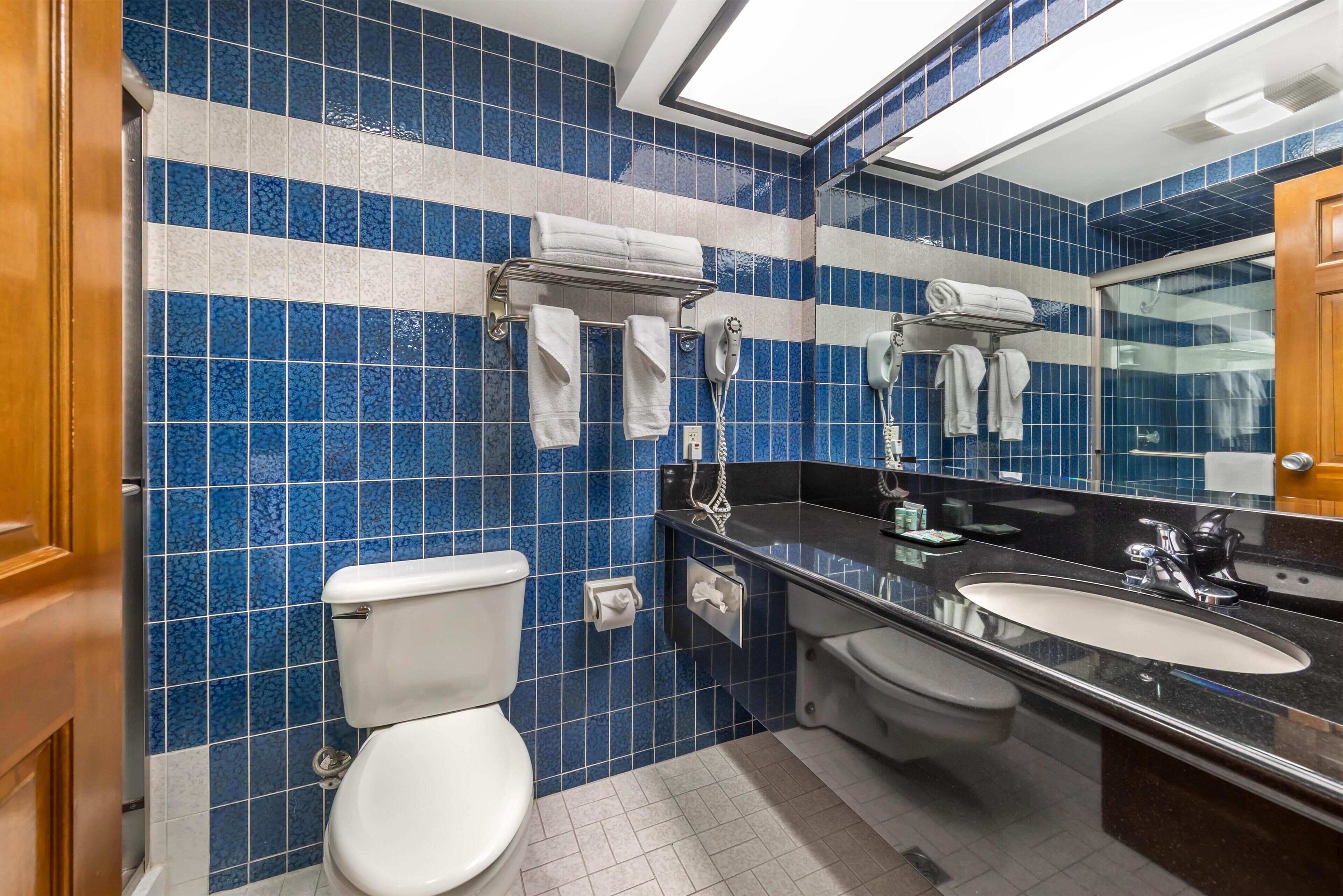 A bathroom with blue tiled walls, a white toilet, a sink, and a mirror.