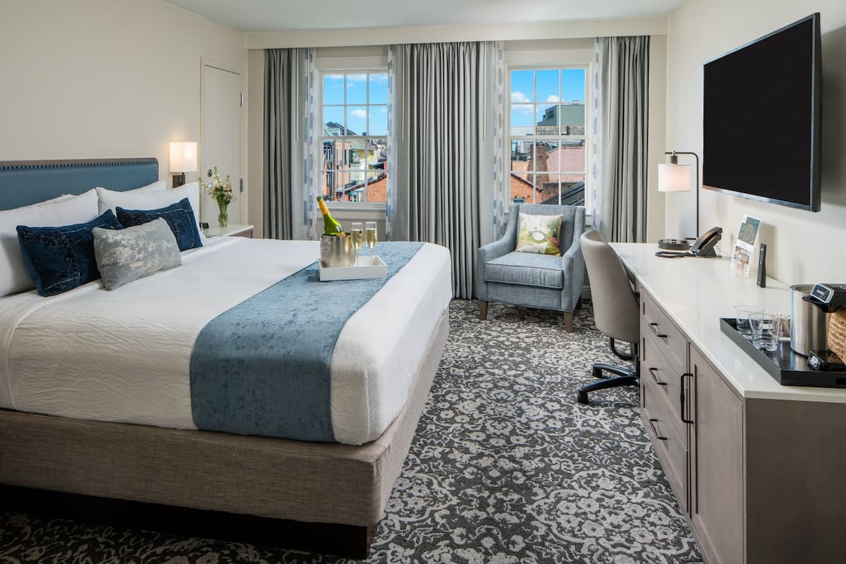 Quarto de hotel com uma cama grande, uma mesa, uma cadeira, televisão de tela plana e vista para prédios pela janela.