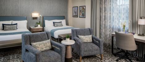 A hotel room with two beds, a desk, a chair, and a small table with a plant.