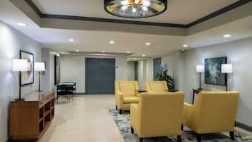 A hotel lobby with a reception desk, two armchairs, a coffee table, a large painting, and a ceiling light fixture.