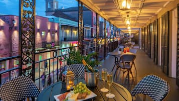 An outdoor terrace with tables and chairs, a bottle of champagne, and a plate of food.