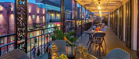 Una terraza exterior con mesas y sillas, una botella de champán y un plato de comida.