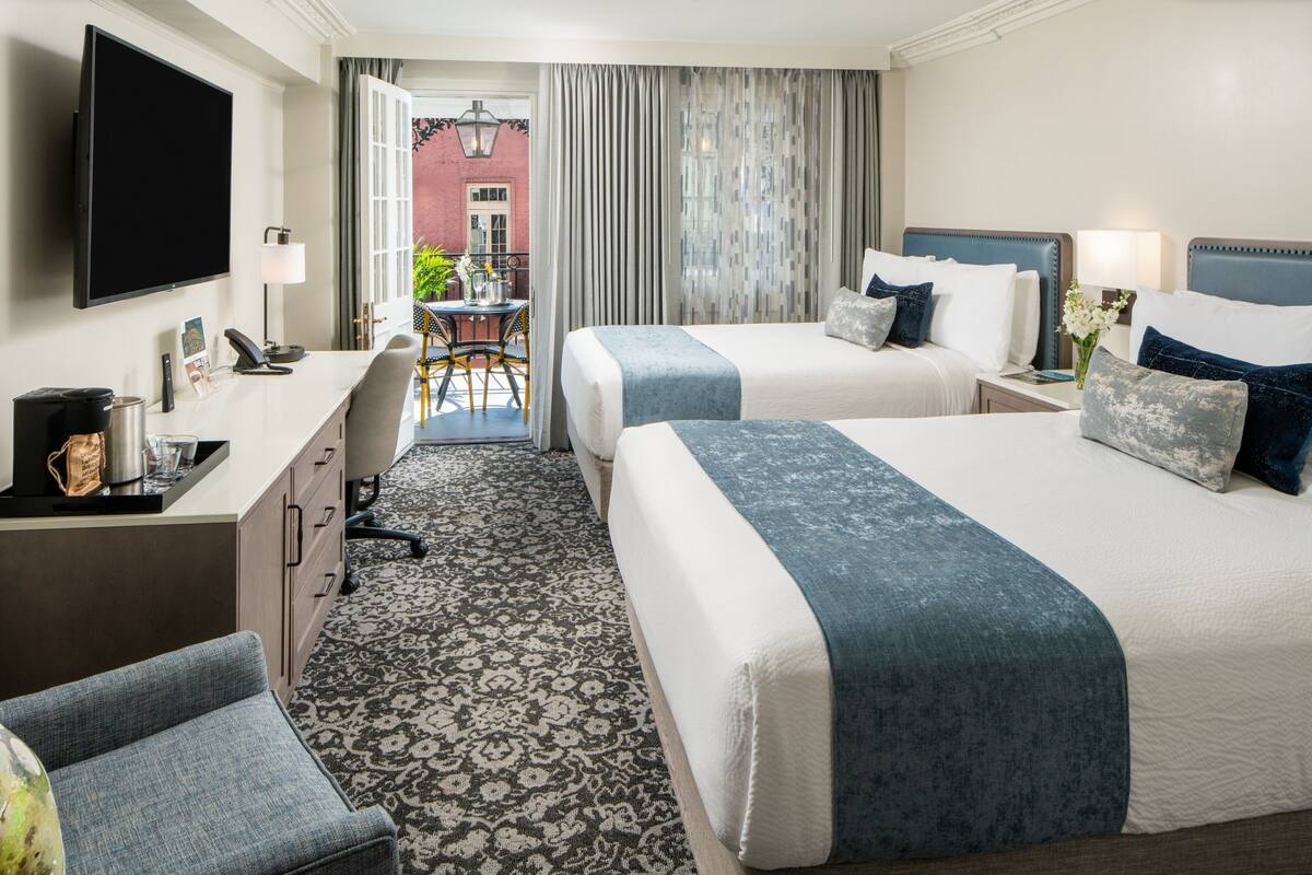 Quarto de hotel com duas camas, uma escrivaninha, uma cadeira, televisão e vista para o exterior.