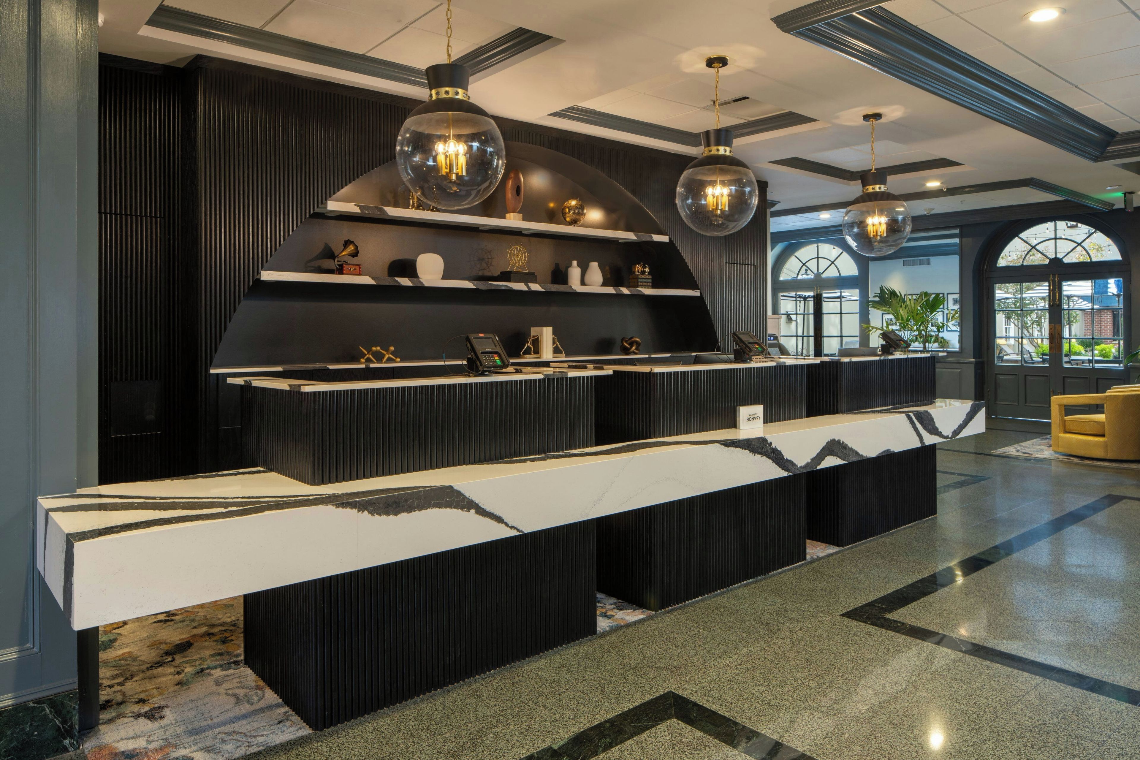 A reception area with a black and white marble counter, pendant lighting, and a view of the outdoors through large windows.