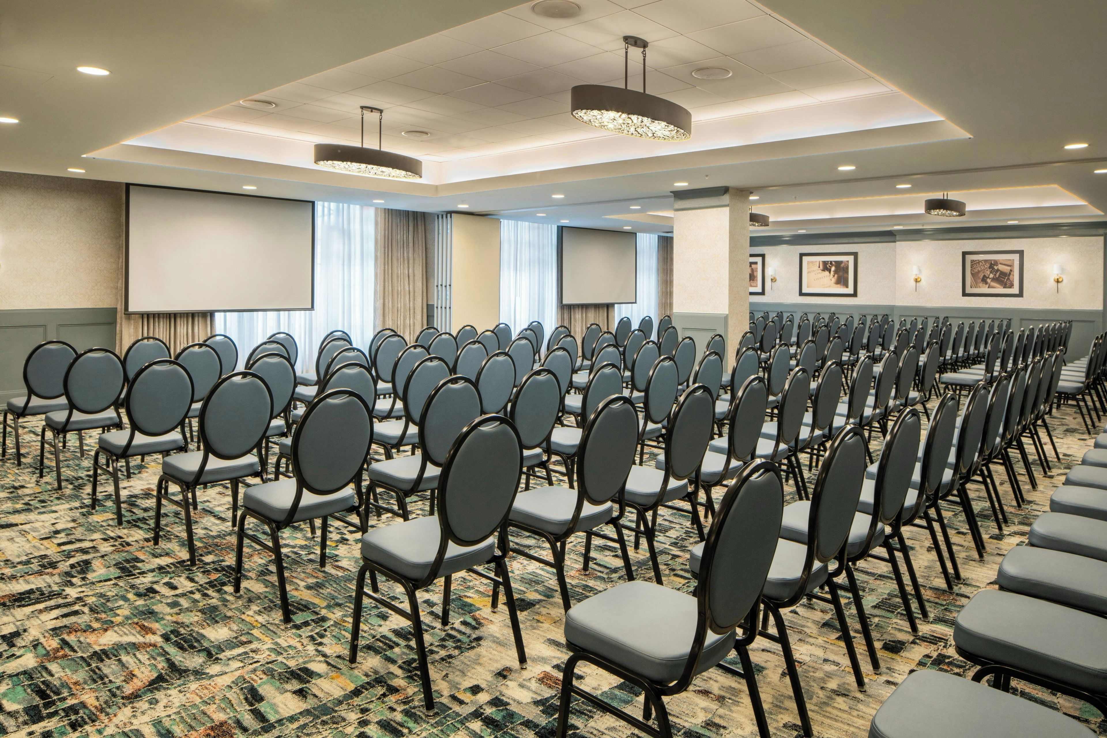 A conference room with rows of chairs, a large screen, and a patterned carpet.
