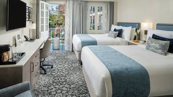 A hotel room with two beds, a desk with a chair, a television, and a view of the outside.