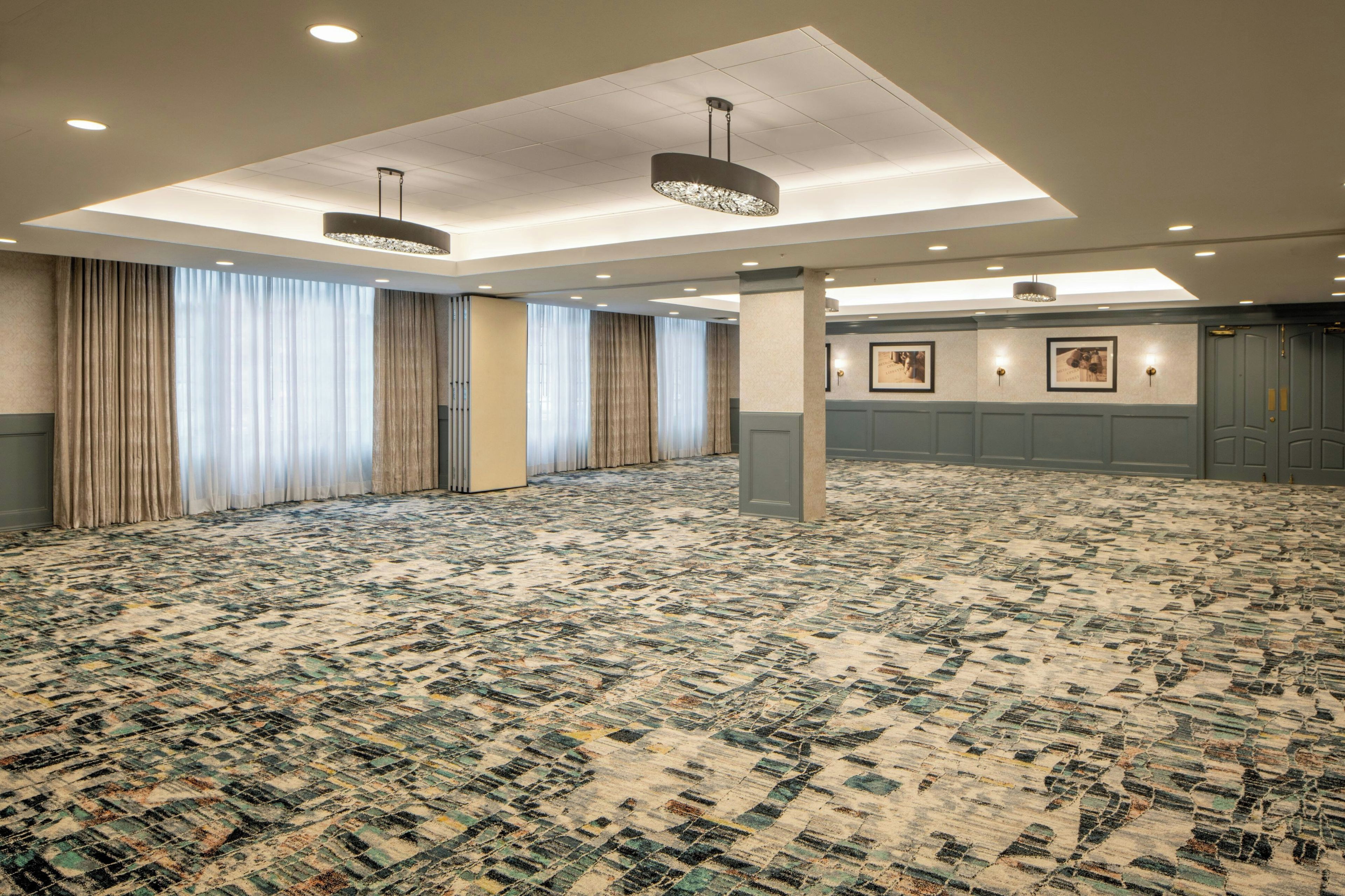 A spacious conference room with patterned carpet, large windows with curtains, and ceiling lights.