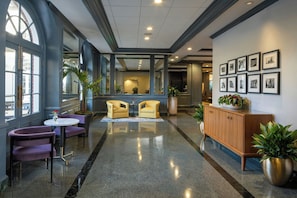 A lobby with a marble floor, yellow armchairs, a wooden cabinet, and framed pictures on the wall. - Four Points By Sheraton French Quarter (New Orleans)