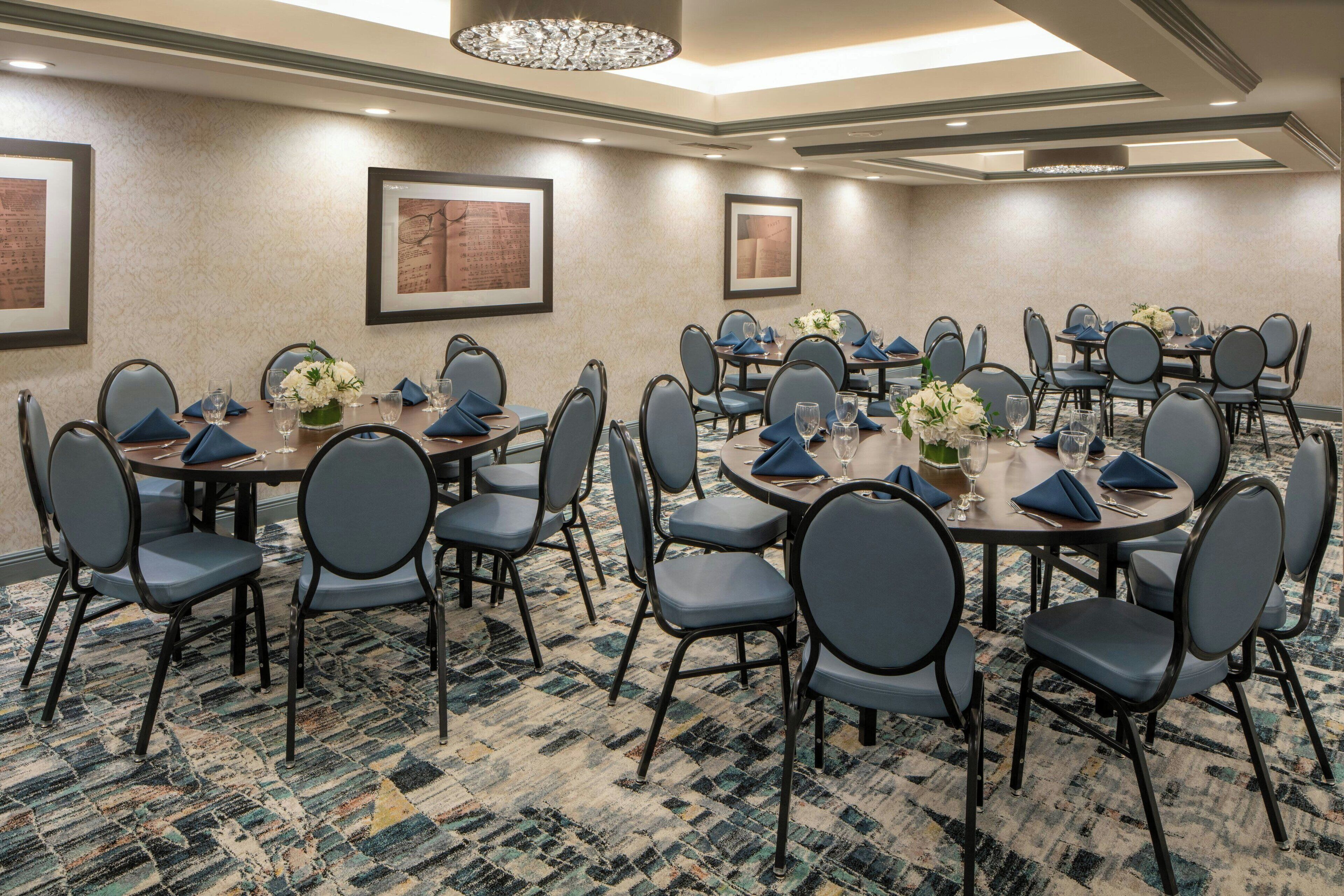 A conference room with round tables, blue chairs, and framed artwork on the walls.