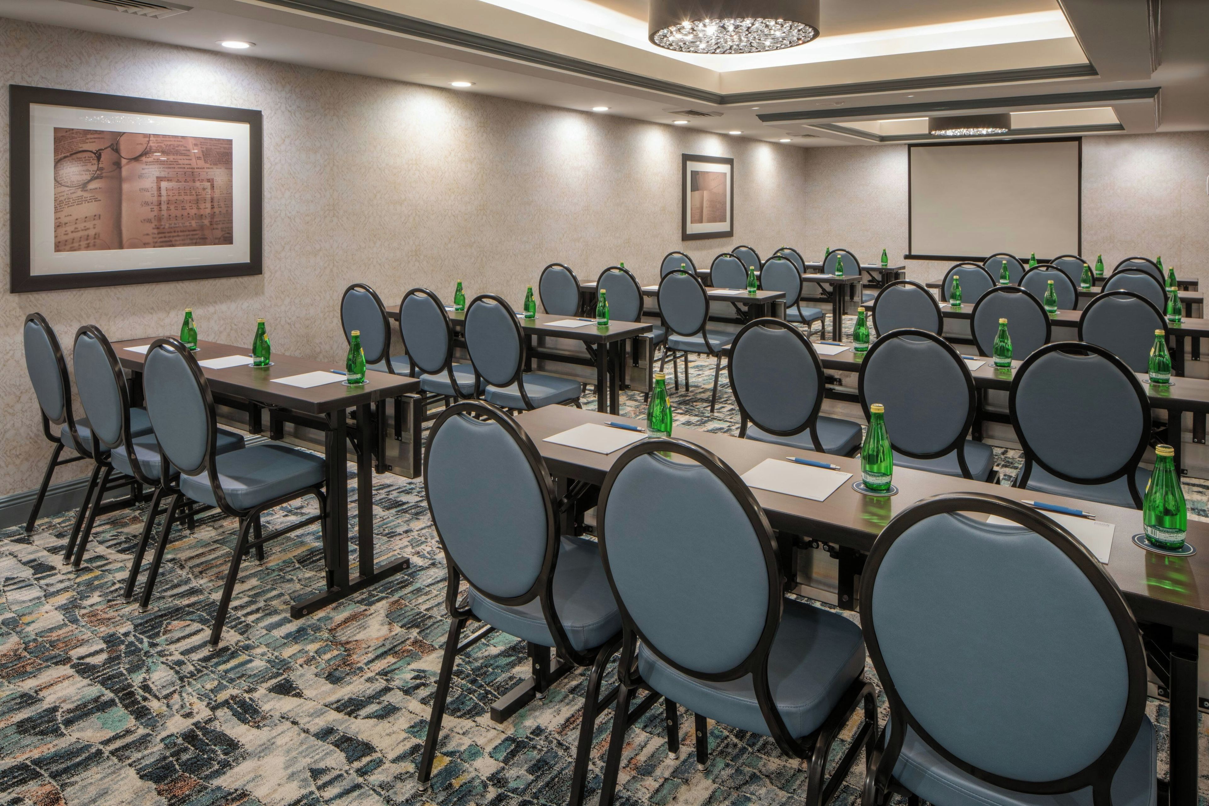 A conference room with multiple tables and chairs, equipped with water bottles and papers.