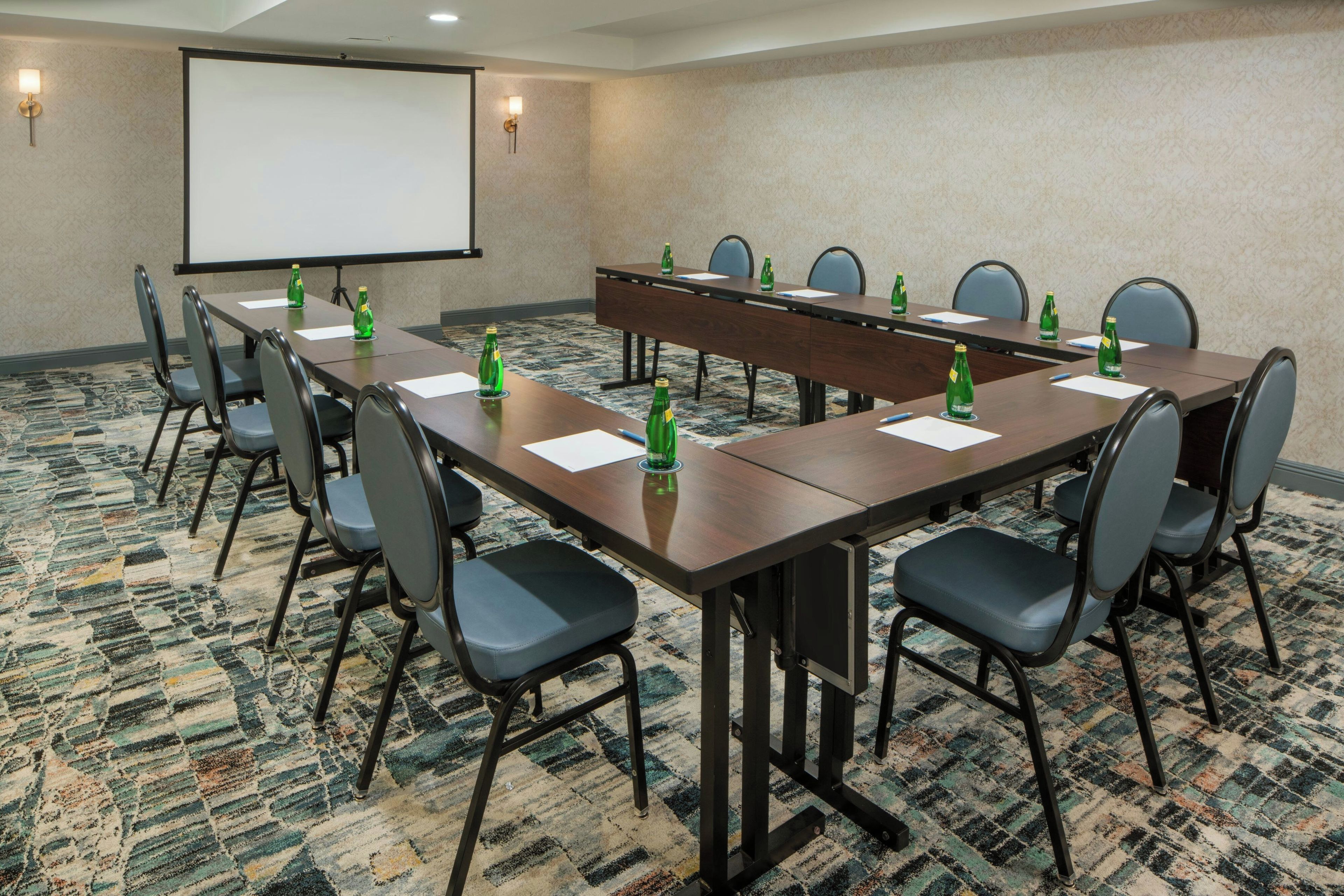A conference room with a long table, chairs, a projector screen, and water bottles.