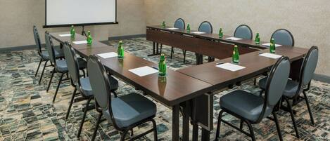 A conference room with a long table, chairs, a projector screen, and water bottles.
