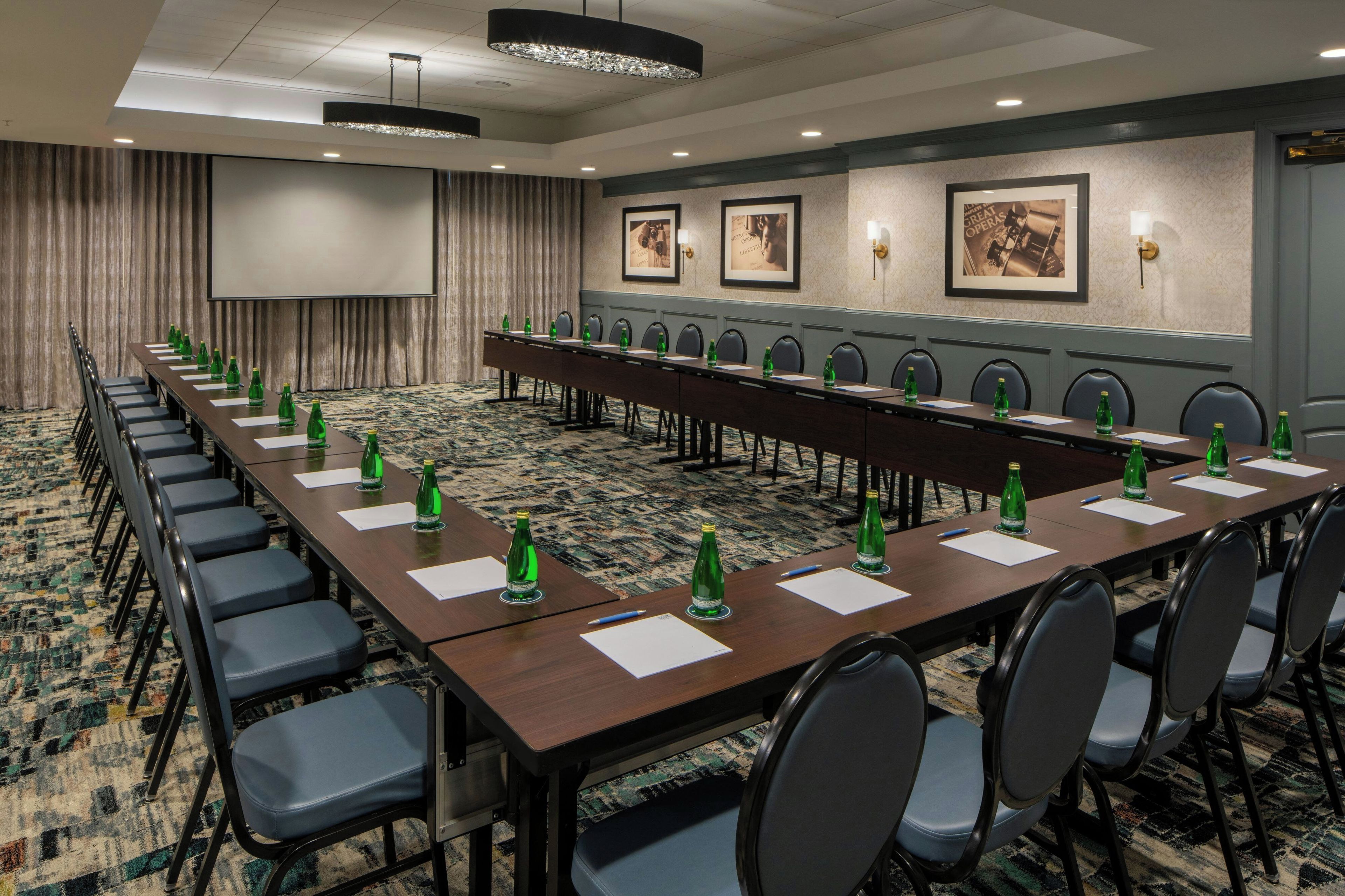 A conference room with a long table, chairs, and a projector screen.