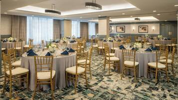 A banquet hall with round tables, gold chairs, and a patterned carpet.