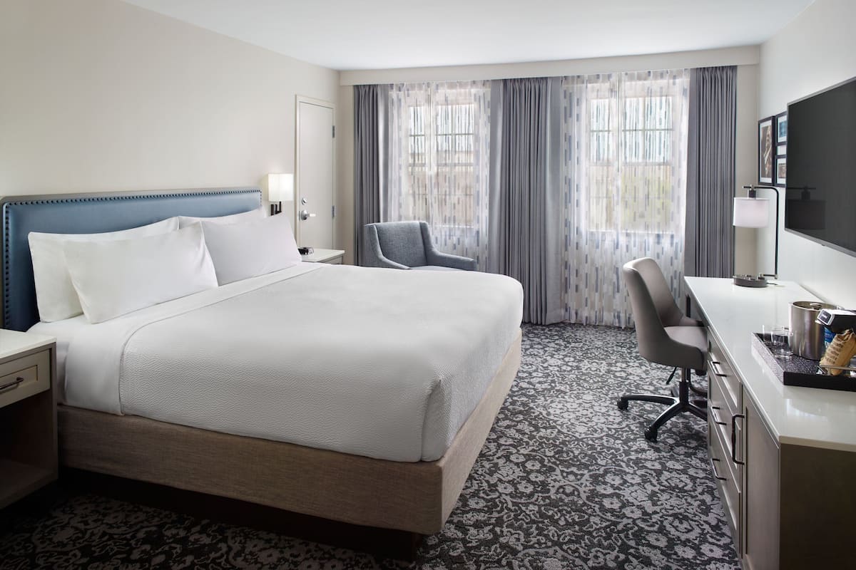 Quarto de hotel com cama grande, escrivaninha, cadeira e televisão.