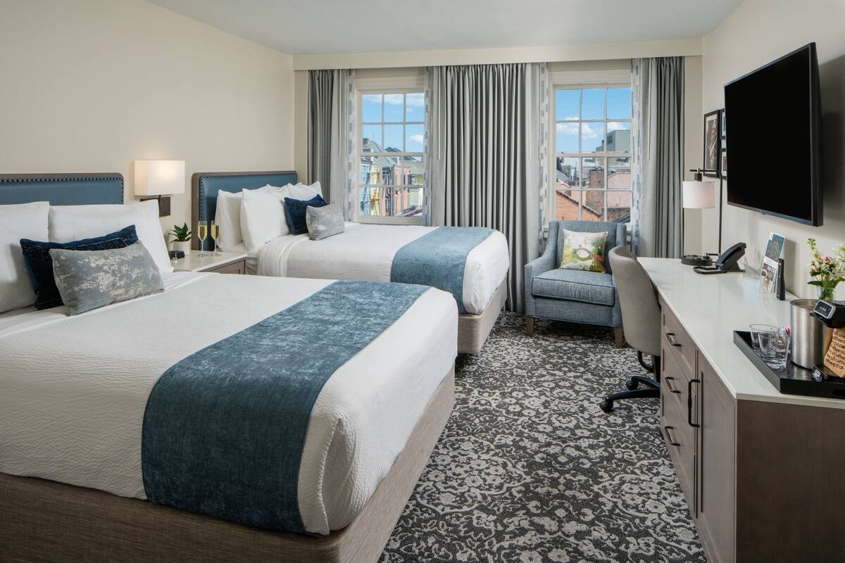Quarto de hotel com duas camas, uma escrivaninha, uma cadeira, televisão e vista para a cidade.