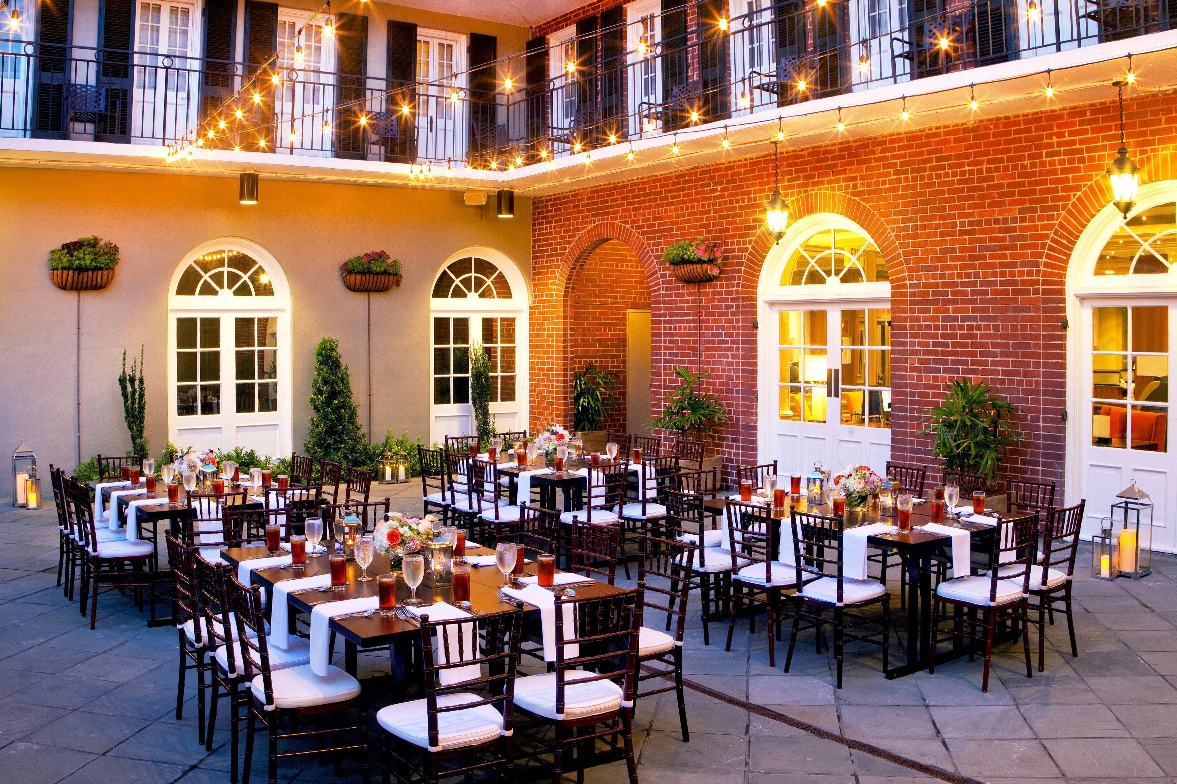 An outdoor dining area with multiple tables and chairs, string lights, and potted plants.