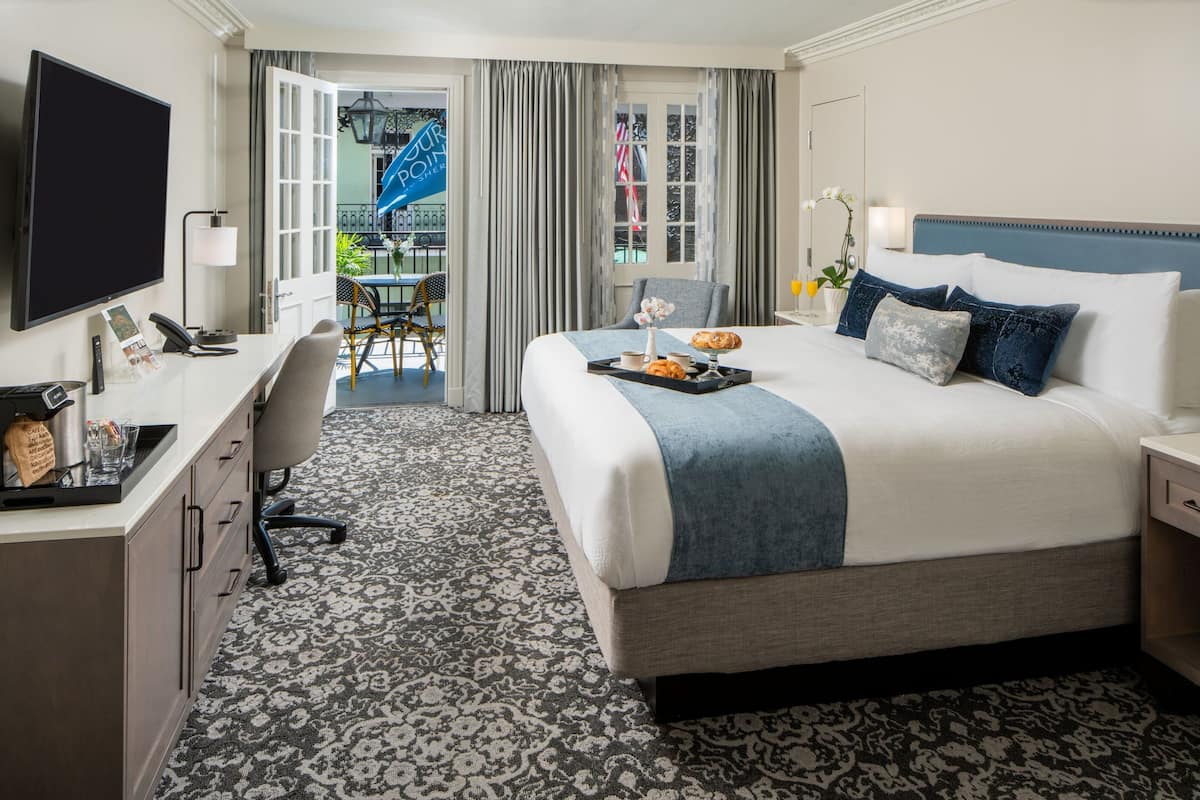 Quarto de hotel com uma cama grande, uma escrivaninha com computador, uma cadeira e vista para a varanda.