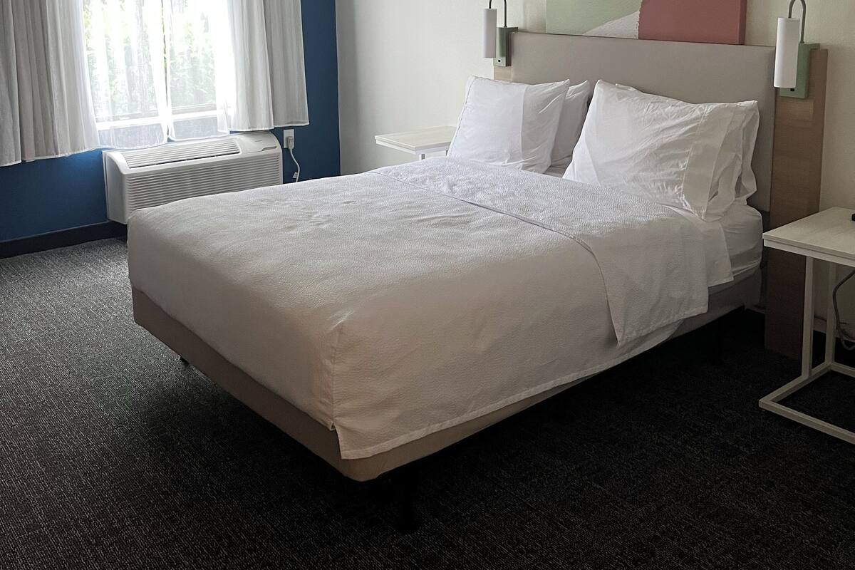 Une chambre d’hôtel avec un grand lit, une table de chevet, un radiateur et une fenêtre avec des rideaux.