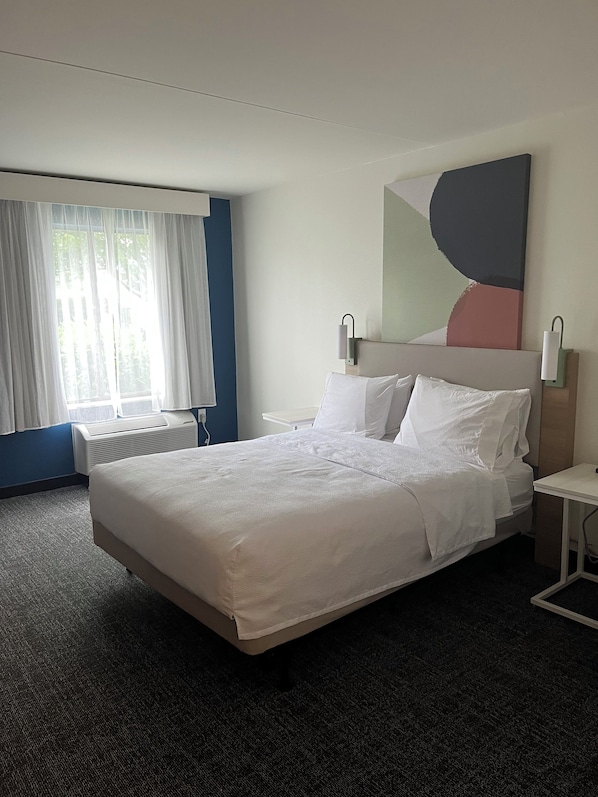 Habitación de hotel con una cama grande, una mesita de noche, un radiador y una ventana con cortinas.