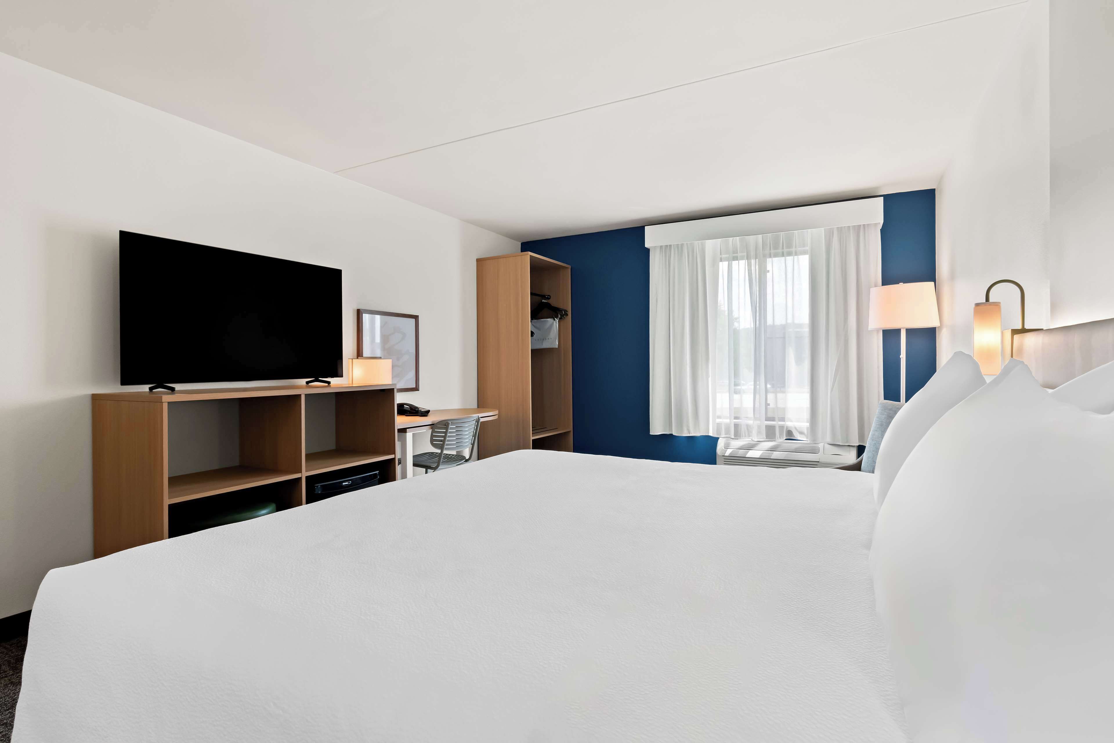Habitación de hotel con una cama grande, un escritorio con silla, televisor, armario y ventana con cortinas.
