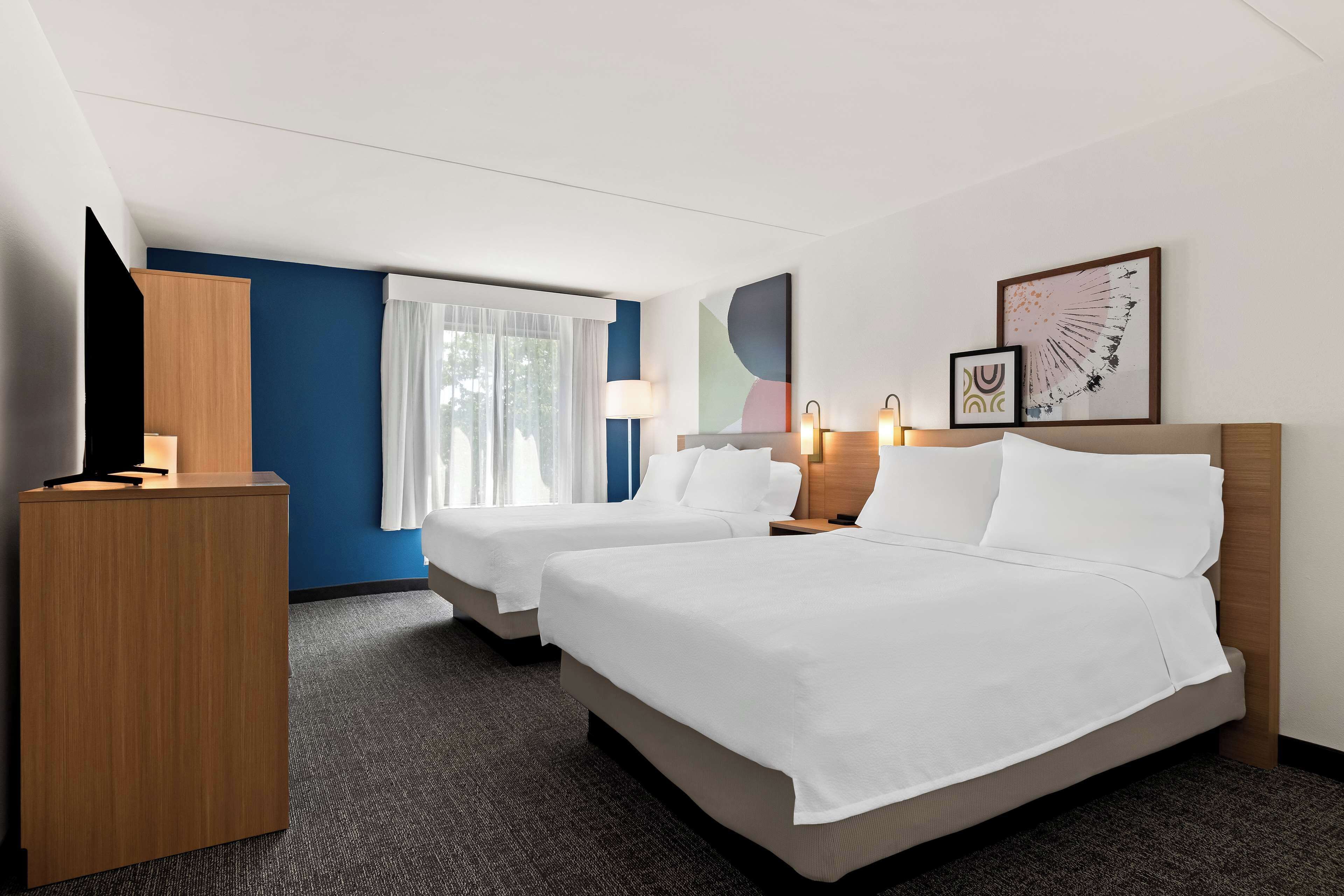 A hotel room with two beds, a desk, a TV, and artwork on the walls.