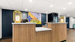 A reception desk with a wooden finish, a large poster, and a vending machine. - Spark by Hilton Hummelstown Hershey (Hummelstown)