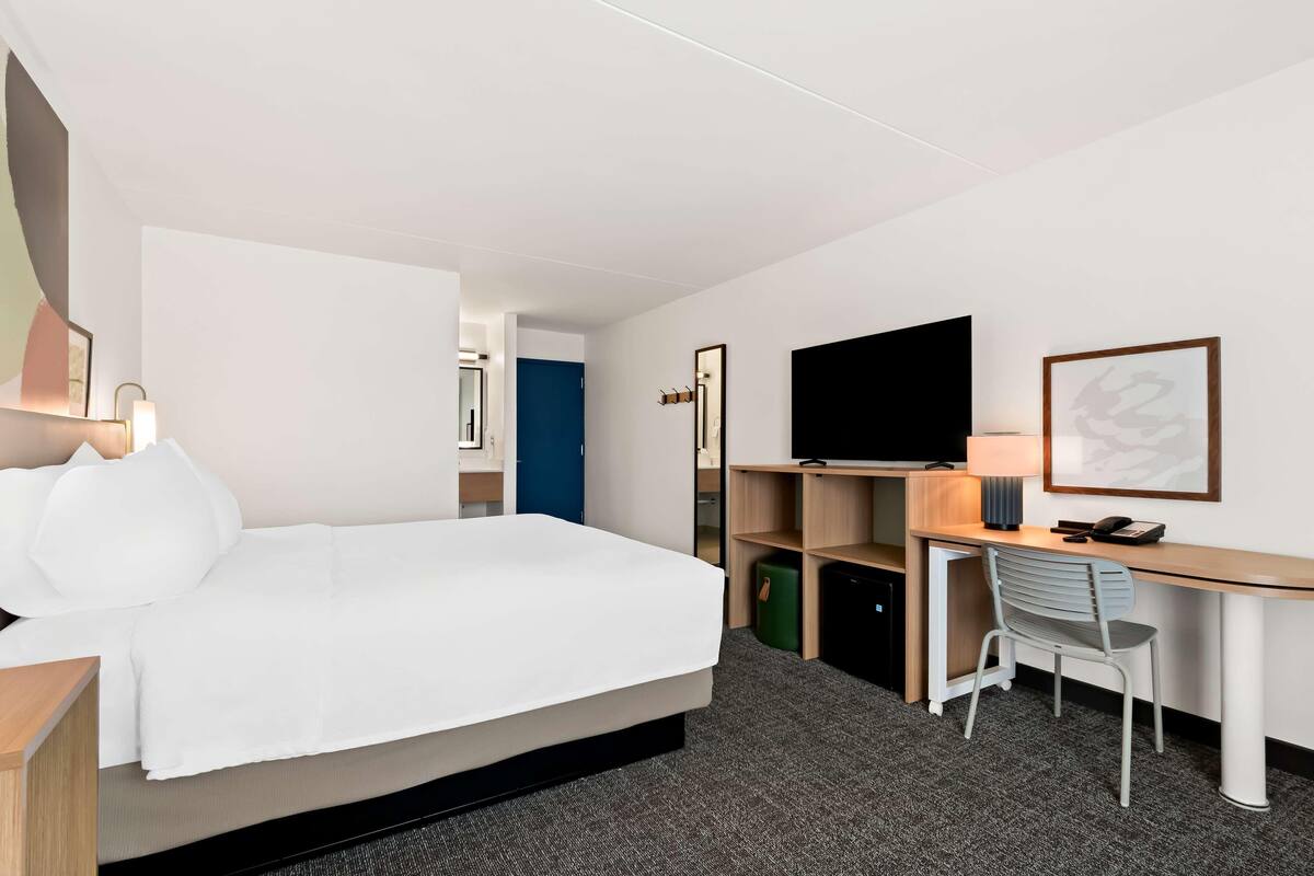 Une chambre d’hôtel comprenant un lit, un bureau, une chaise, une télévision et une porte donnant sur une autre pièce.