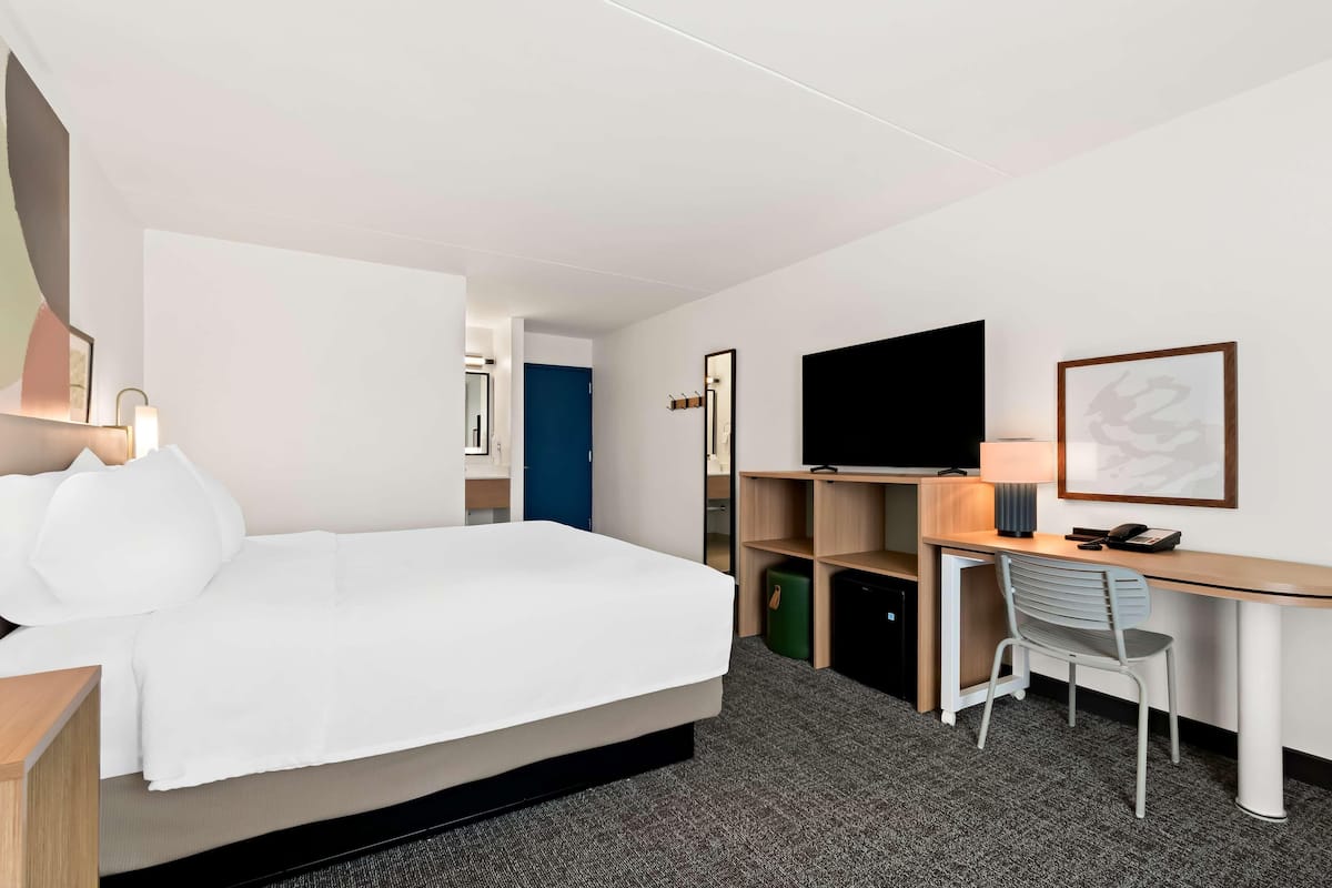 A hotel room with a bed, desk, chair, TV, and a door leading to another room.