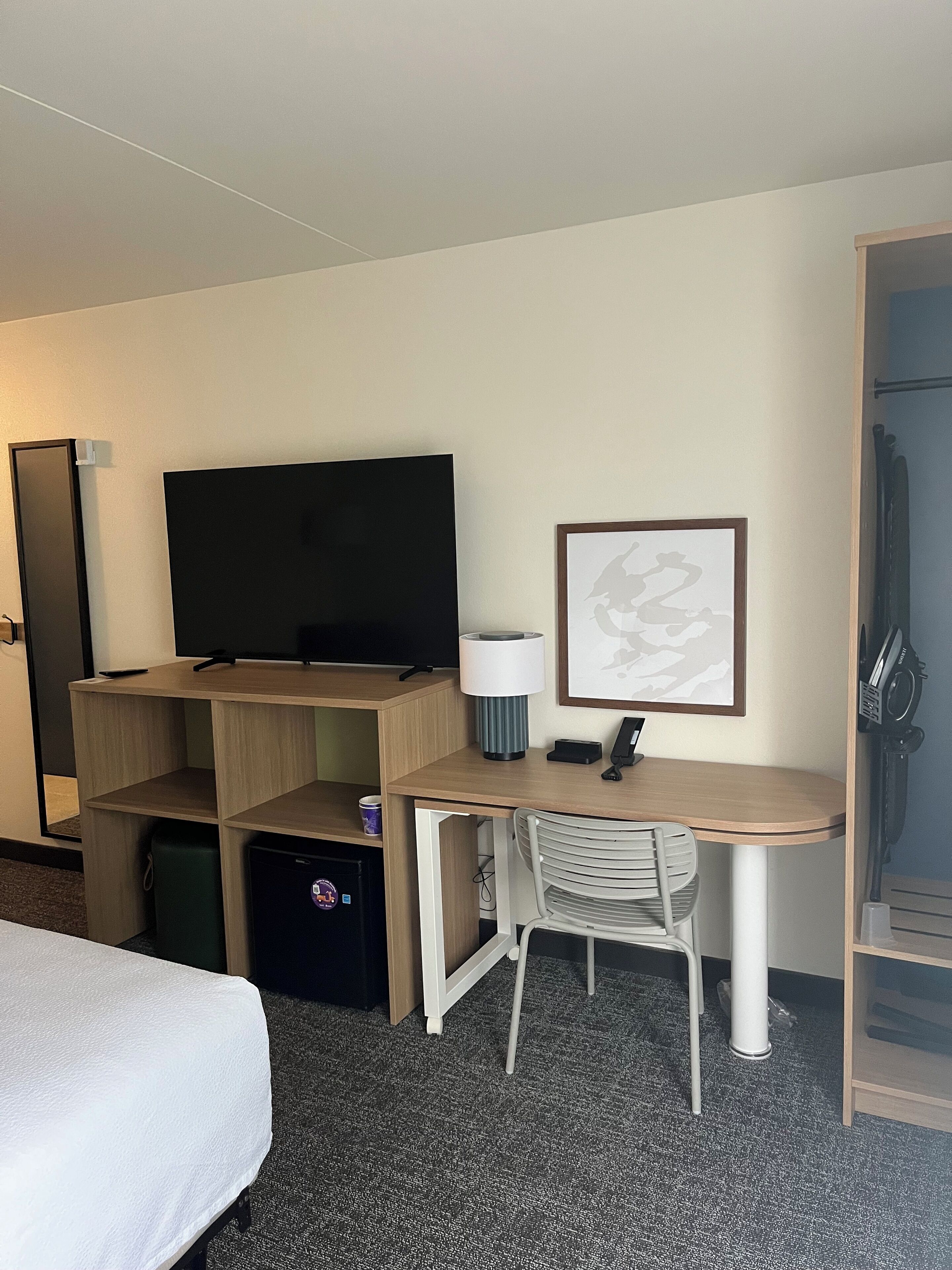 Habitació d'hotel amb un llit, una taula de treball amb una cadira, una televisió, una làmpada i un quadre a la paret.
