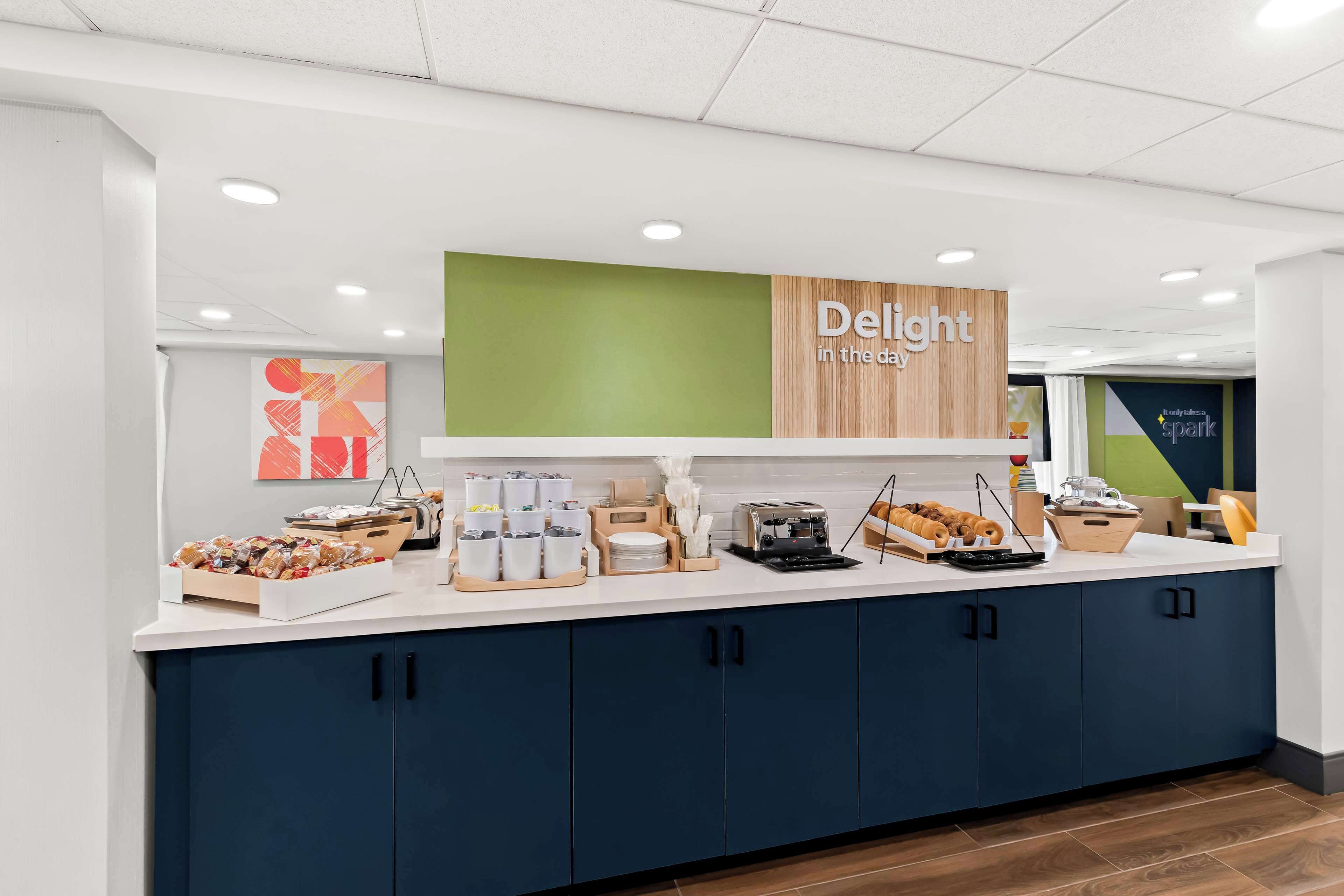 A breakfast bar with a sign reading "Delight in the day," featuring a variety of pastries and breakfast items.