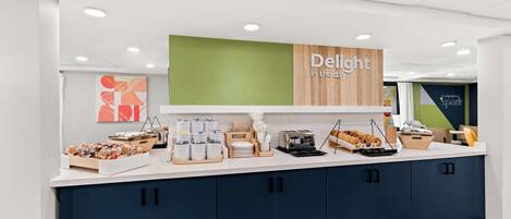 A breakfast bar with a sign reading "Delight in the day," featuring a variety of pastries and breakfast items.