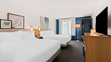 A hotel room with two beds, a desk, a TV, and artwork on the walls.