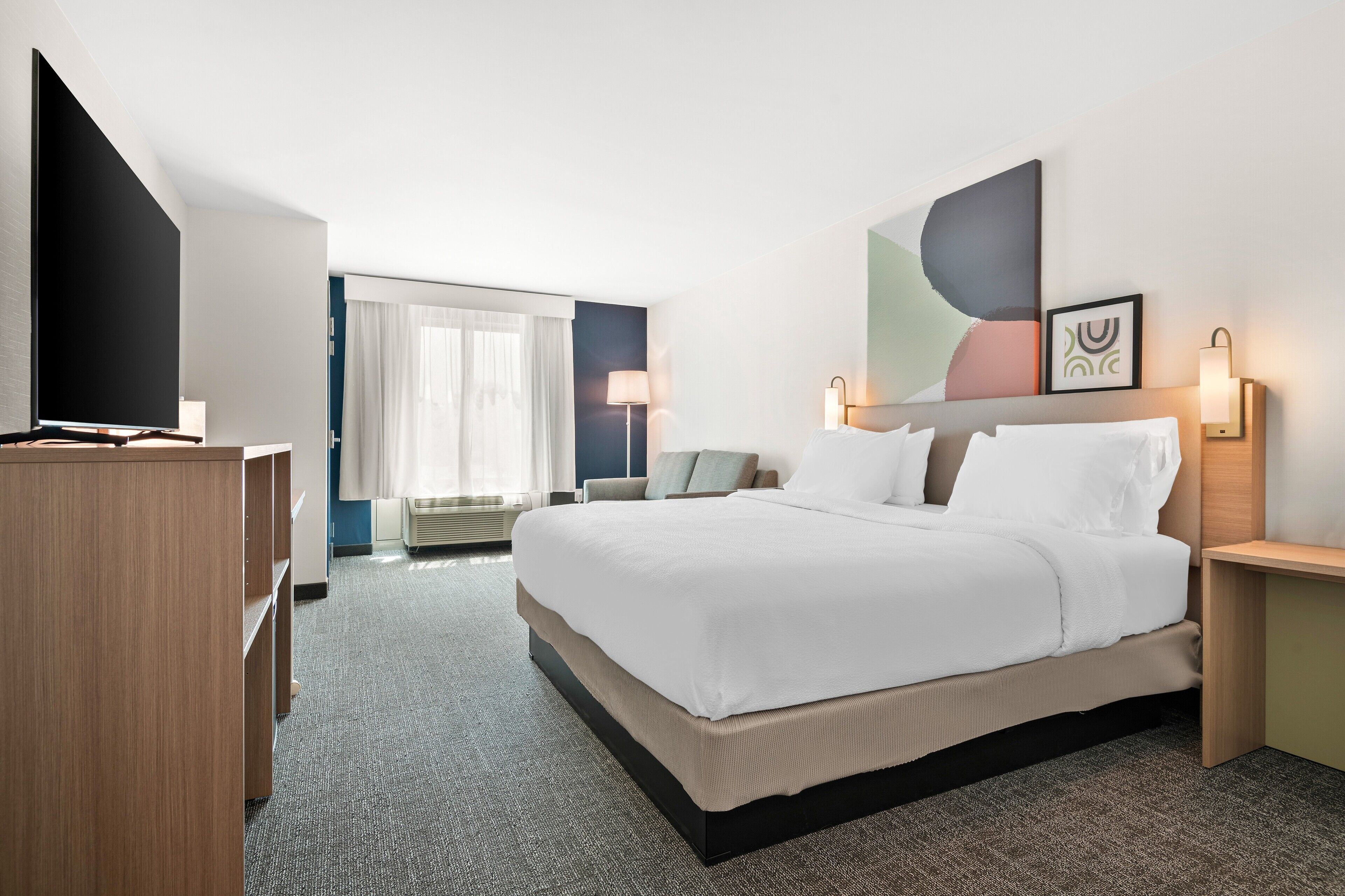 A hotel room with a large bed, a flat-screen TV, a desk, and a window with curtains.