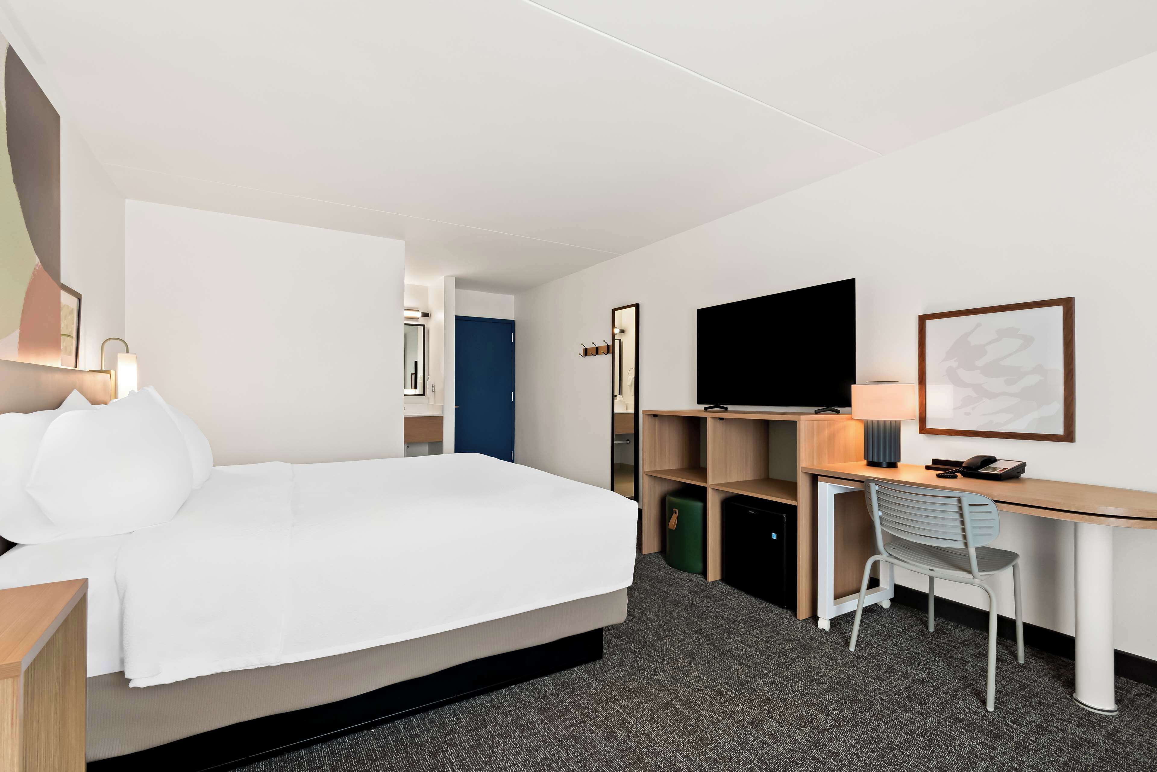 Habitación de hotel con cama, escritorio, silla, televisión y puerta que da a otra habitación.