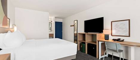 Habitación de hotel con cama, escritorio, silla, televisión y puerta que da a otra habitación.