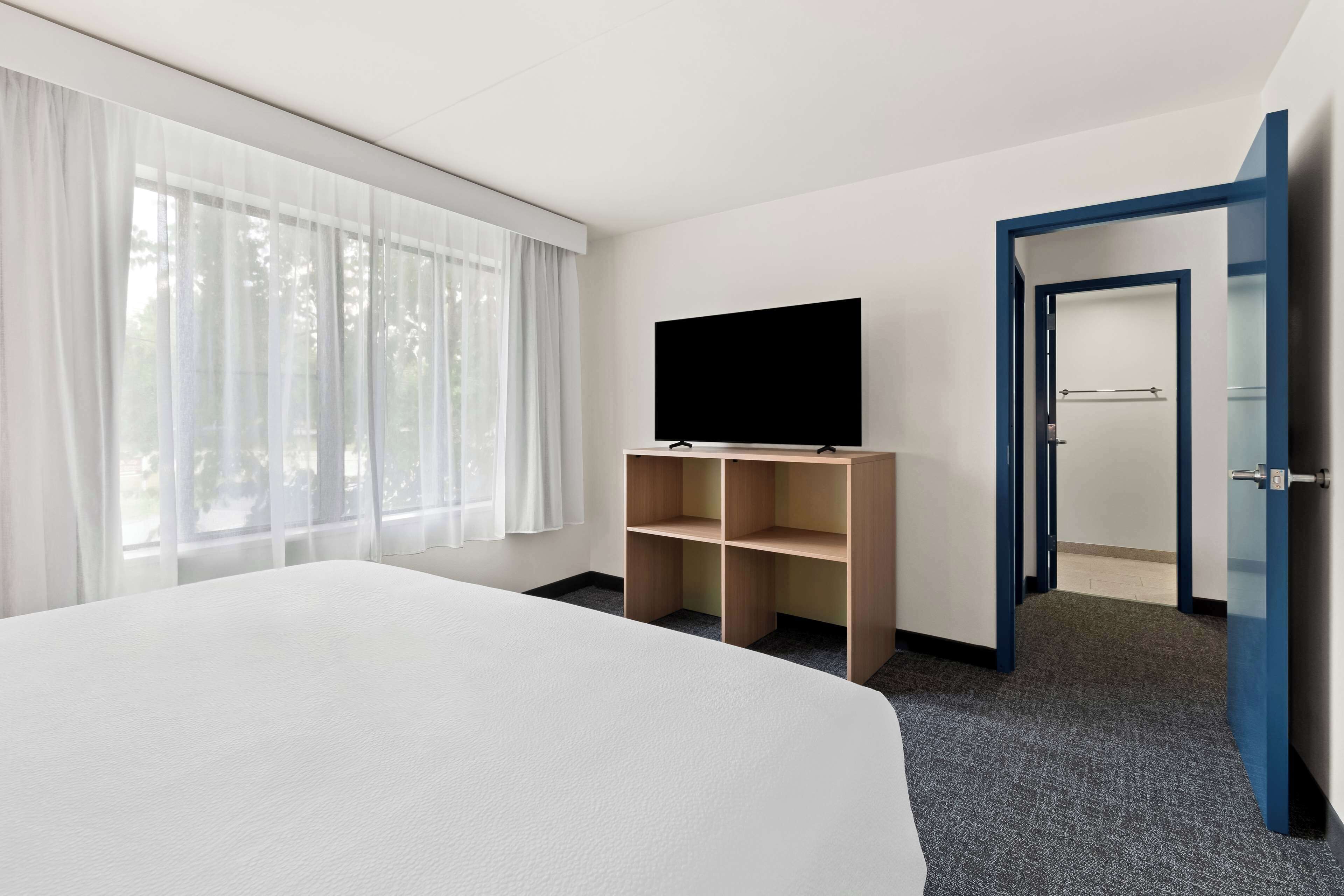 A hotel room with a large bed, a television on a wooden stand, and a door leading to another room.