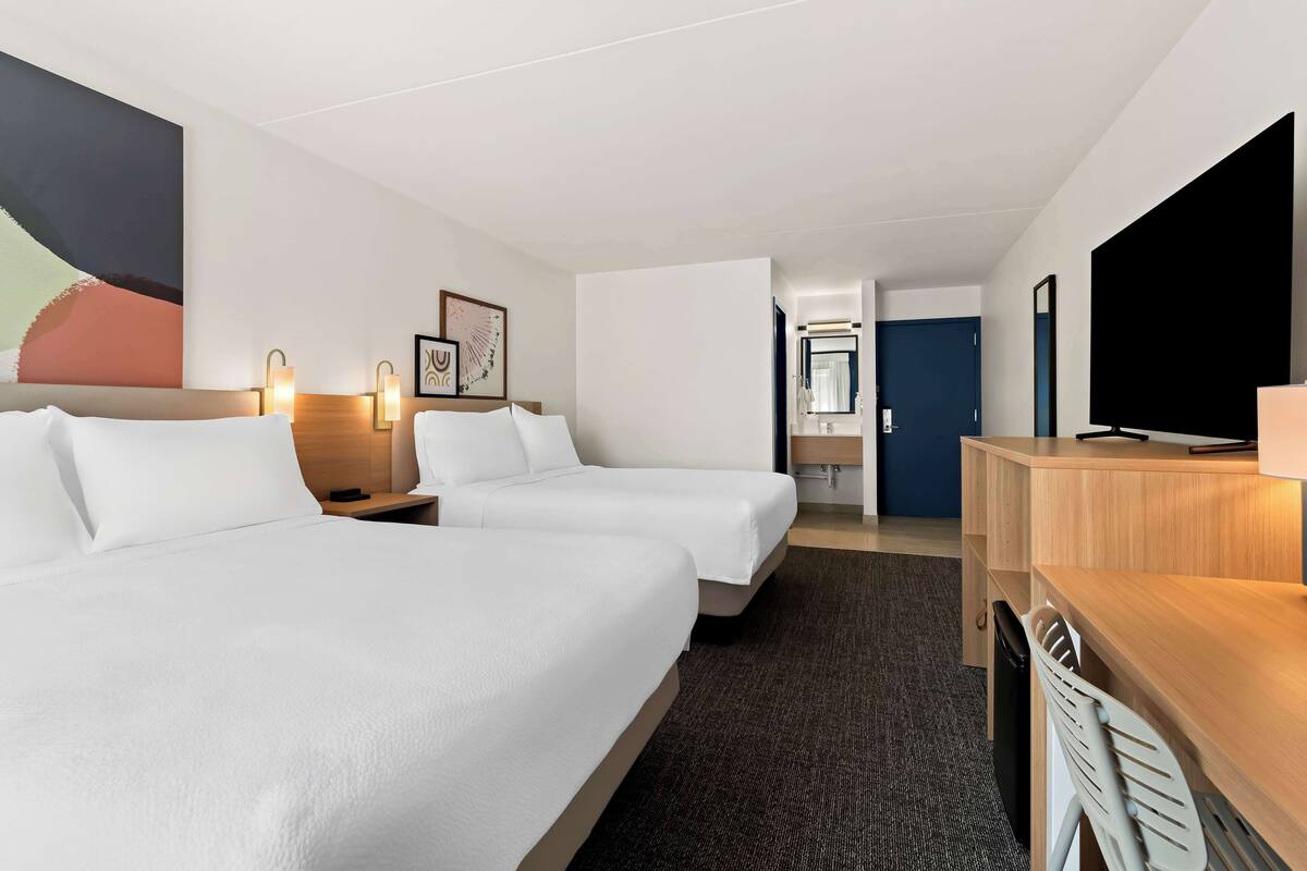 Une chambre d’hôtel avec deux lits, un bureau, une télévision et une salle de bain visible au fond.