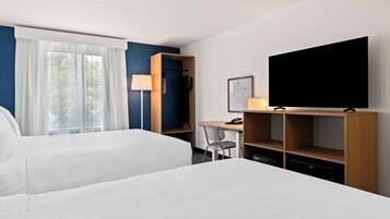 Habitación de hotel con dos camas, un escritorio, una silla, un televisor y un armario.