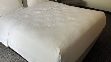 Una habitación de hotel con una cama grande, una mesita, una silla, una lámpara y una pared decorada con un cuadro geométrico.