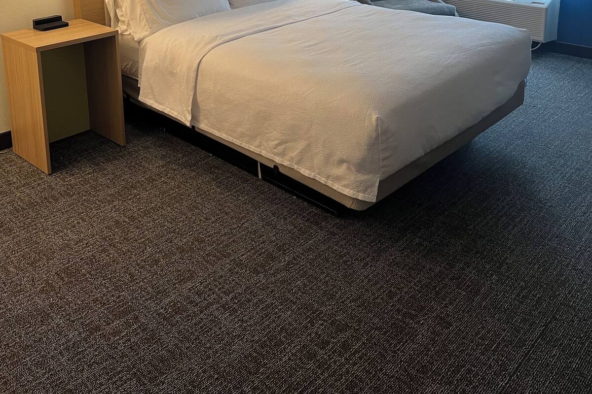 Une chambre d’hôtel avec un grand lit, deux tables de chevet, une chaise, une fenêtre avec des rideaux et une œuvre d’art murale.