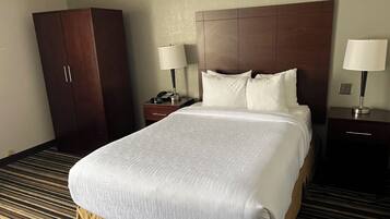A hotel room with a large bed, two bedside tables with lamps, a wardrobe, and a carpeted floor.
